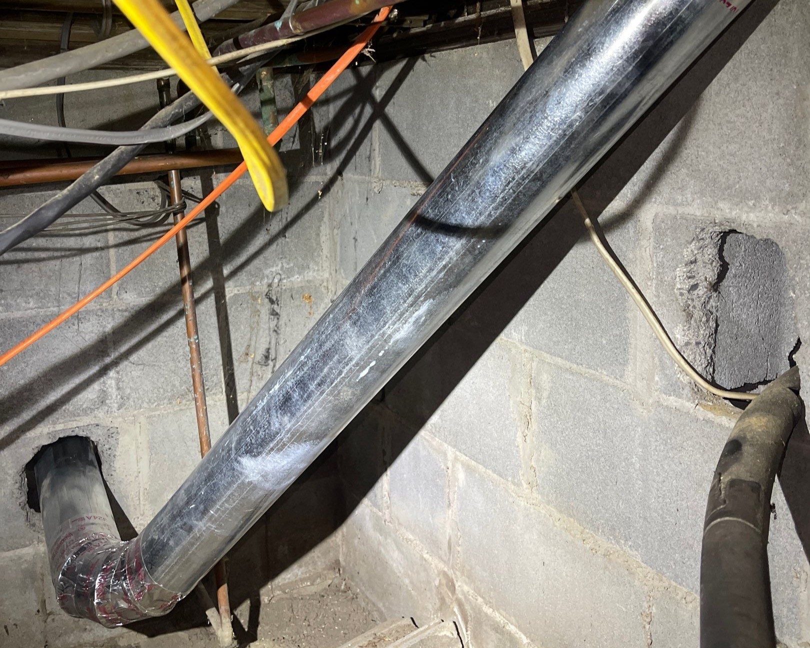 Full metal dryer vent run traced along a basement ceiling and wall through elbows and connections, showing the complete ductwork Voyager cleans from the dryer to the exterior cap.